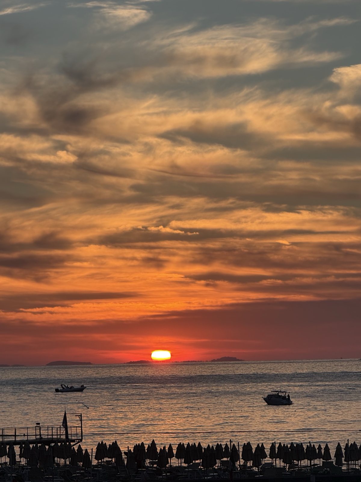 Sunset over the sea, with islands on the horizon and boats in the bay